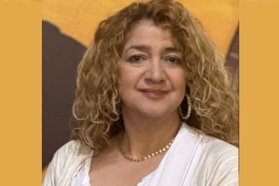 Smiling person with curly hair in a white top against a warm orange background