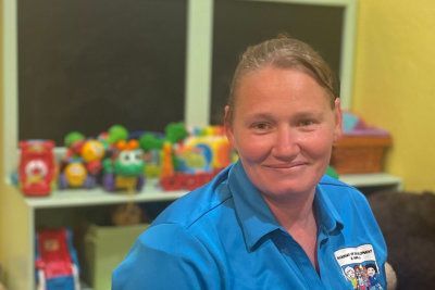 Smiling person in a blue polo shirt in front of a table with colorful toys and a window