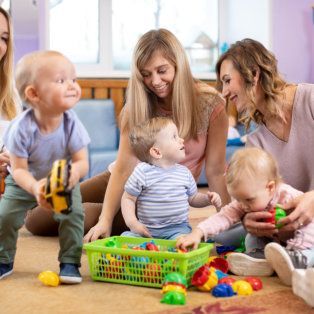 Caregiver and three toddlers playing with colorful toys on a living room floor