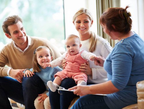 Family sitting together on a couch, smiling and holding a baby in a bright living room