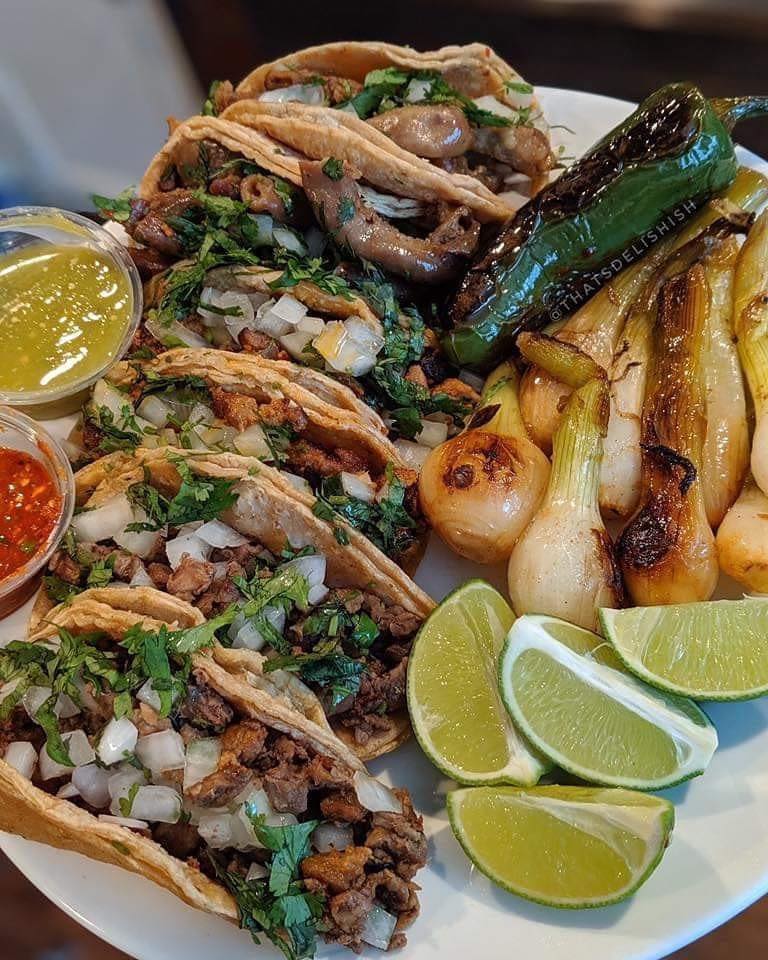 Plate of tacos with grilled onions, peppers, limes, and sauces.