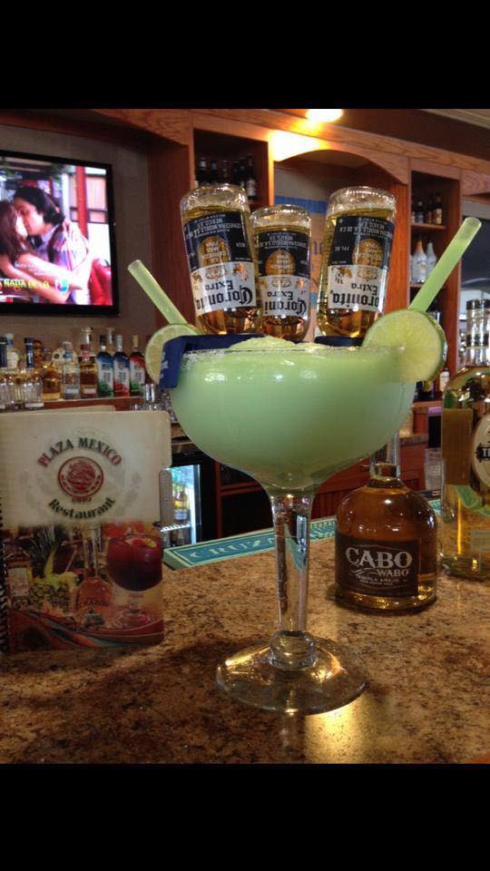 Giant margarita glass with three Corona bottles inverted in it, at a bar.
