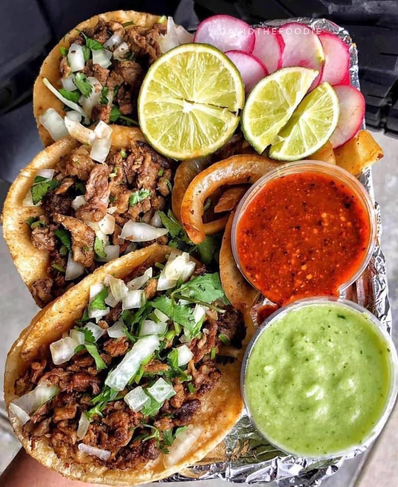 Tacos with meat, onions, cilantro, limes, radishes, onion rings, and red and green salsa.
