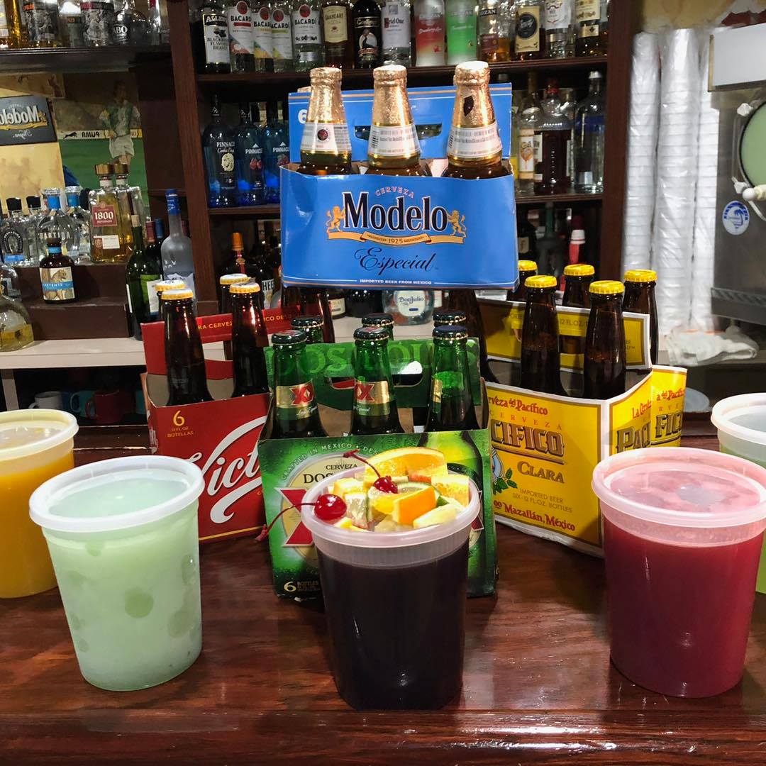 Bar scene with drinks and beer bottles. Cocktails in plastic cups. Shelves of alcohol behind the bar.