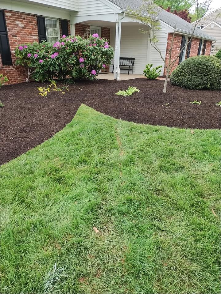 Front yard with green lawn, dark mulch beds, pink flowering shrub, and a white house porch.