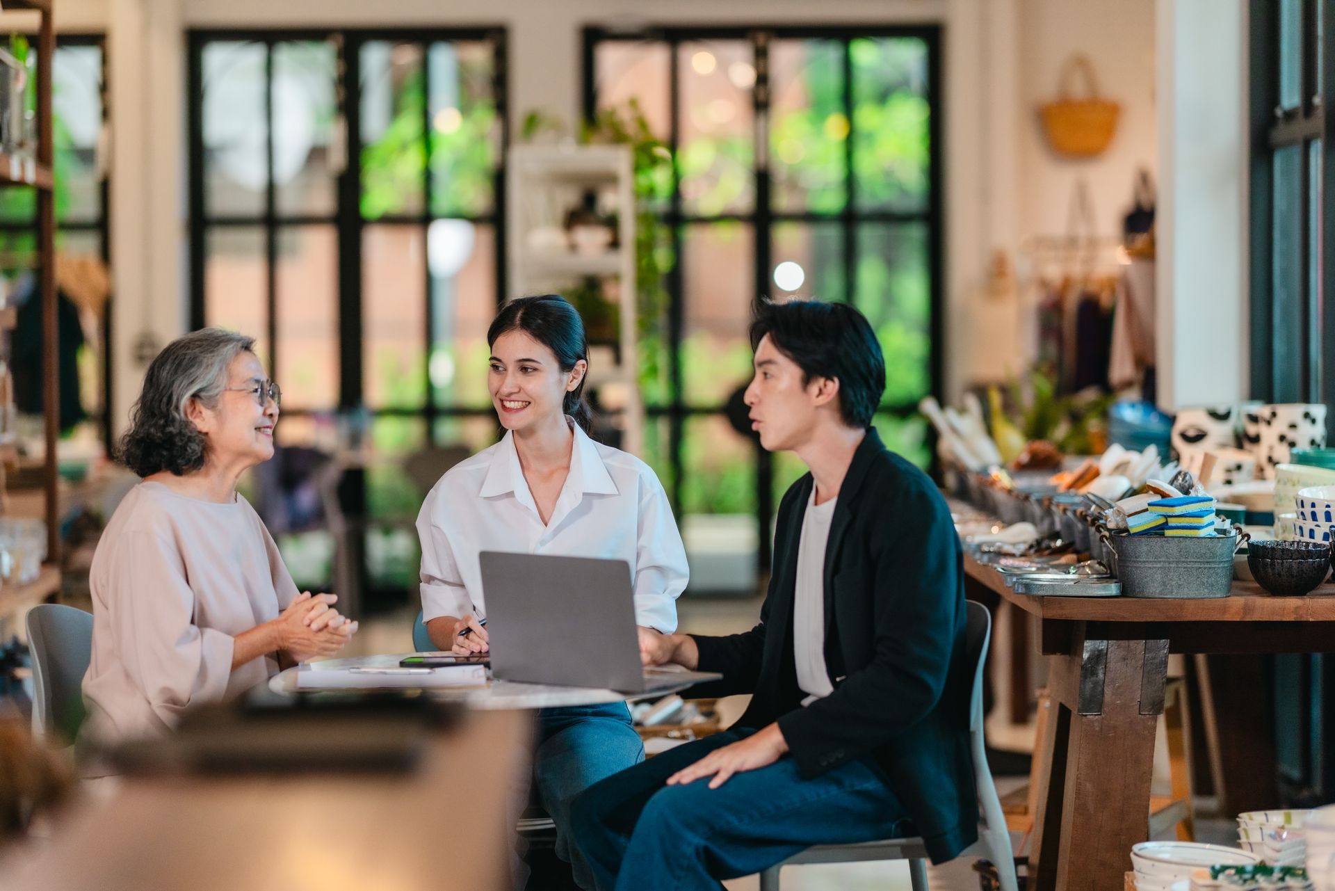 Three people chatting around a laptop in a bright cafe or coworking space