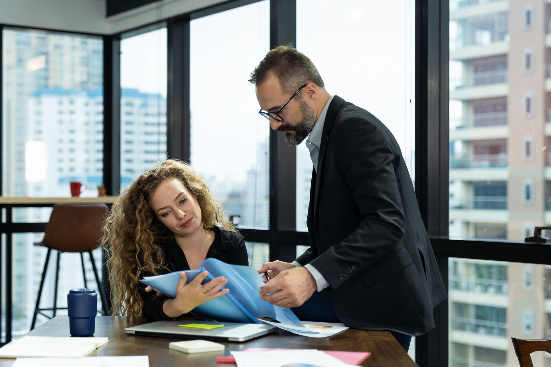 Two colleagues talking in a modern office, with two others blurred in the background.