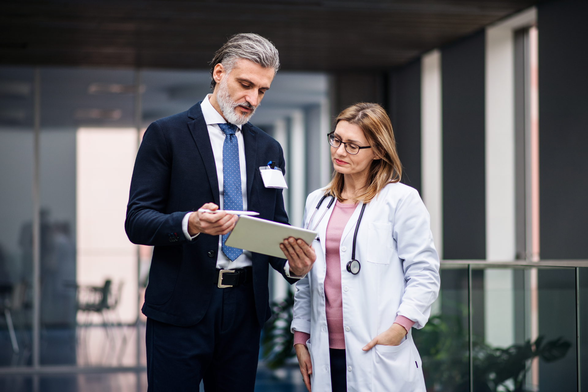 Two professionals in business attire reviewing a tablet outside an office building