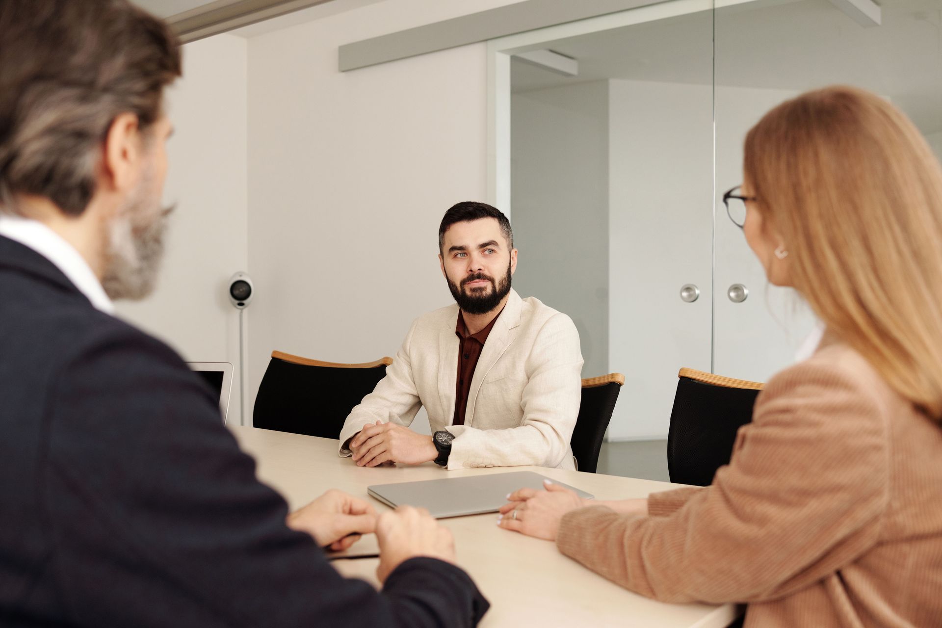 Three people in a meeting room discussing a laptop at a table