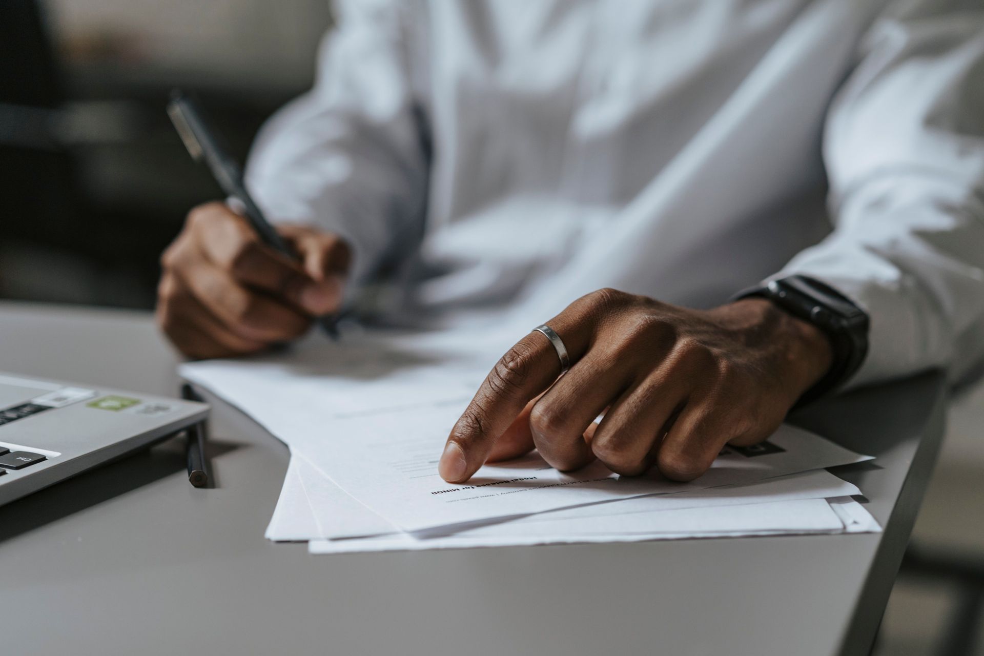 Hands signing a document at a desk with a pen and laptop nearby