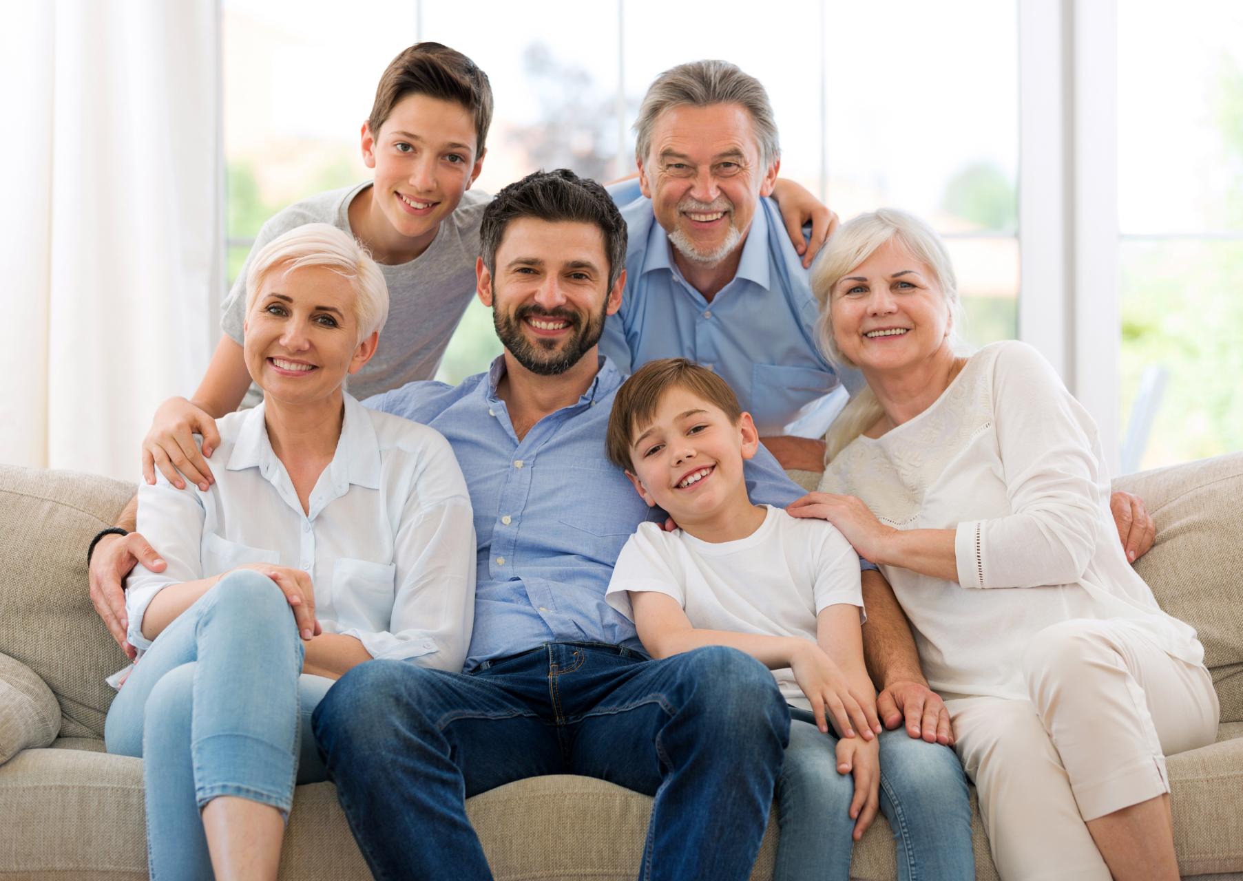 Happy family group sitting on a couch in a bright living room, smiling at the camera