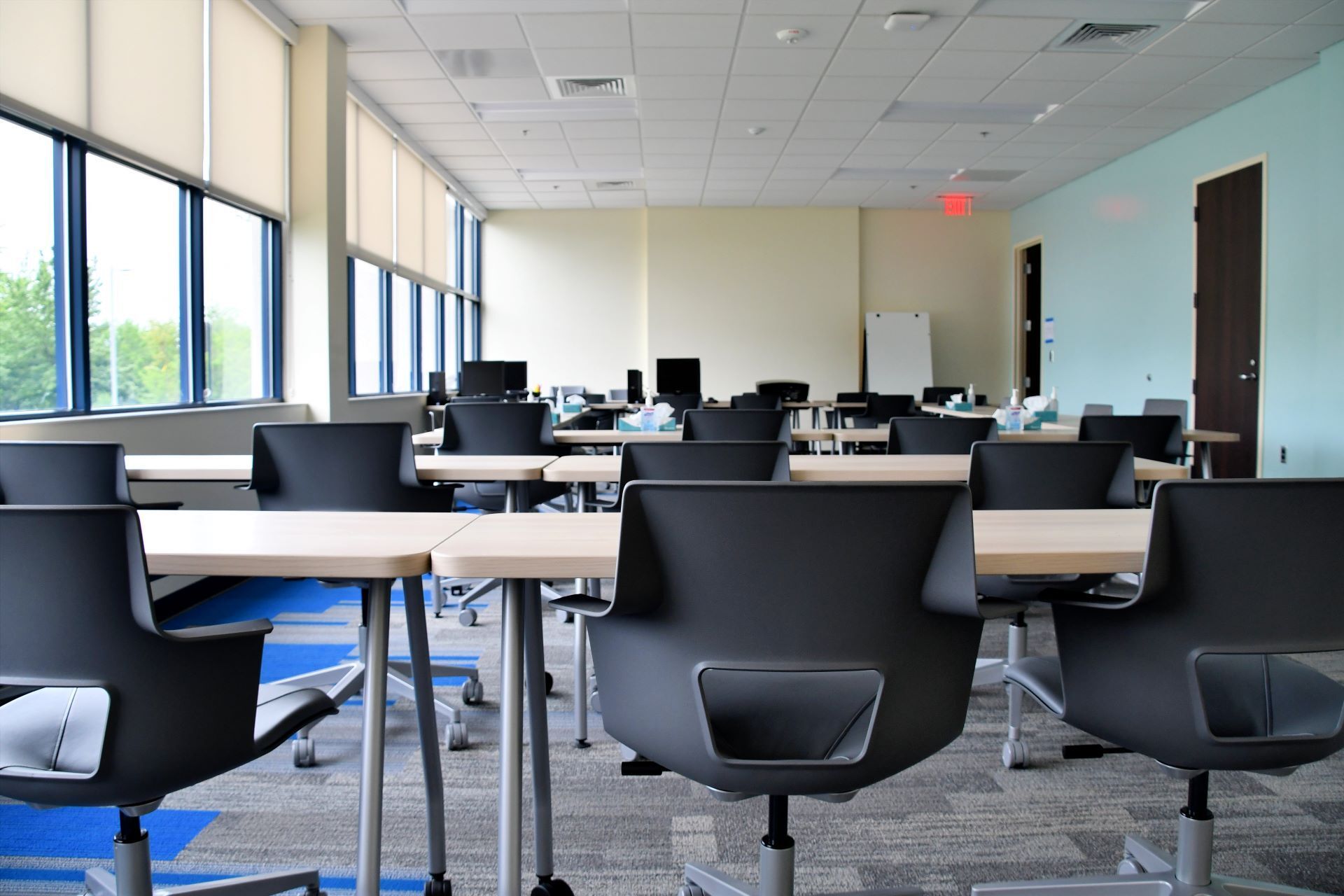 A classroom with tables and chairs and a red exit sign