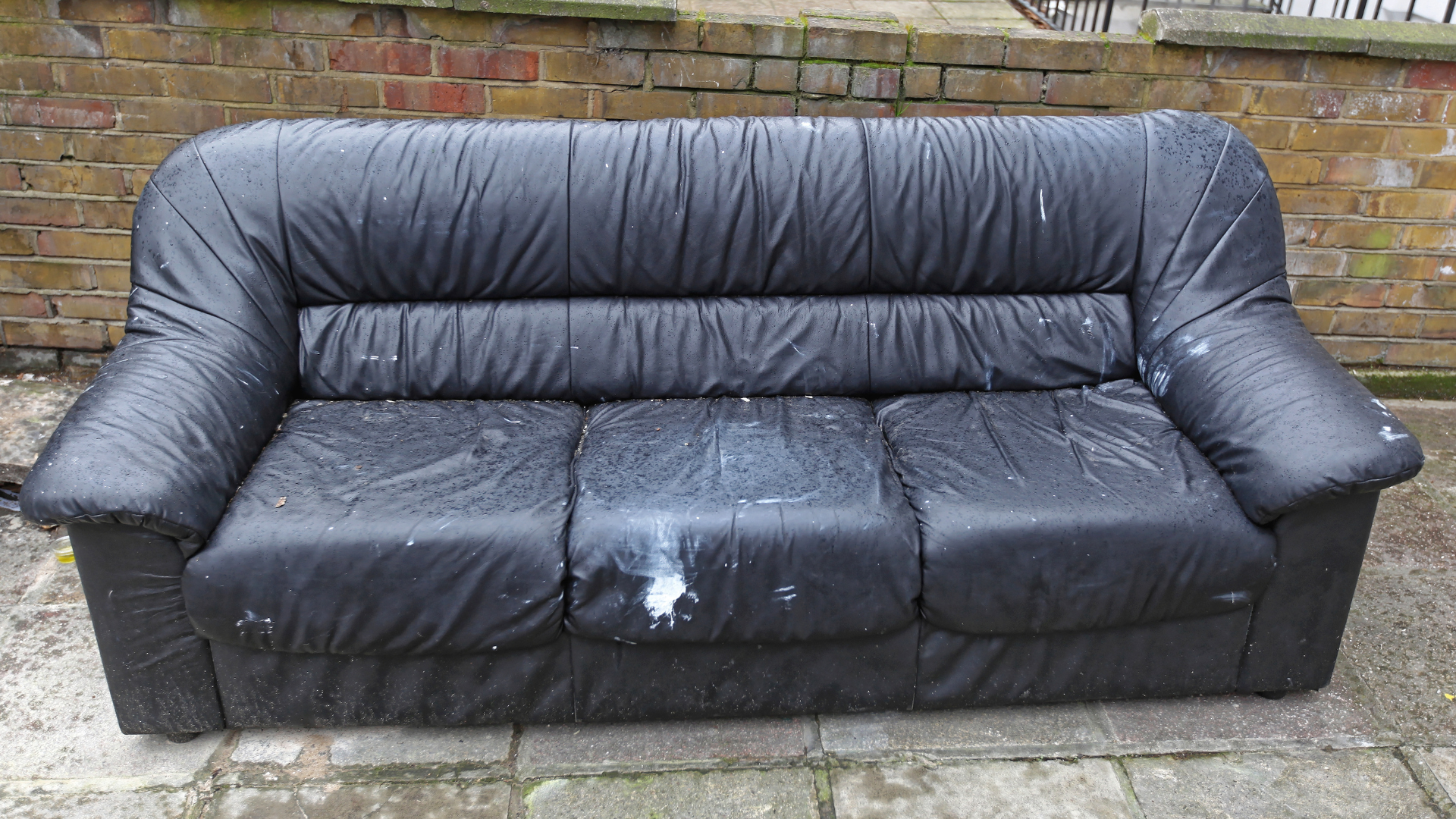 A black leather couch is sitting in front of a brick wall