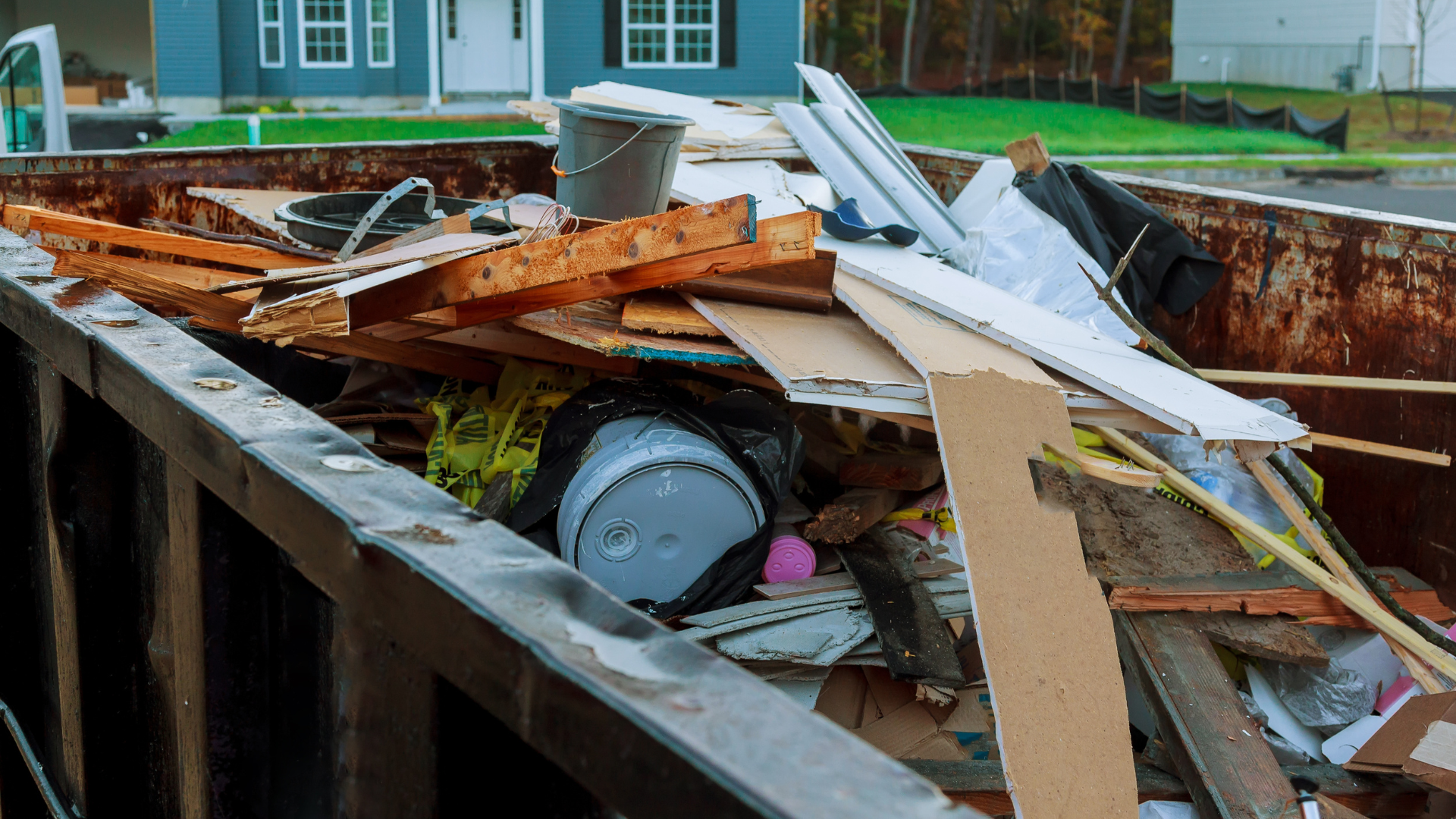 A dumpster filled with lots of junk in front of a house.