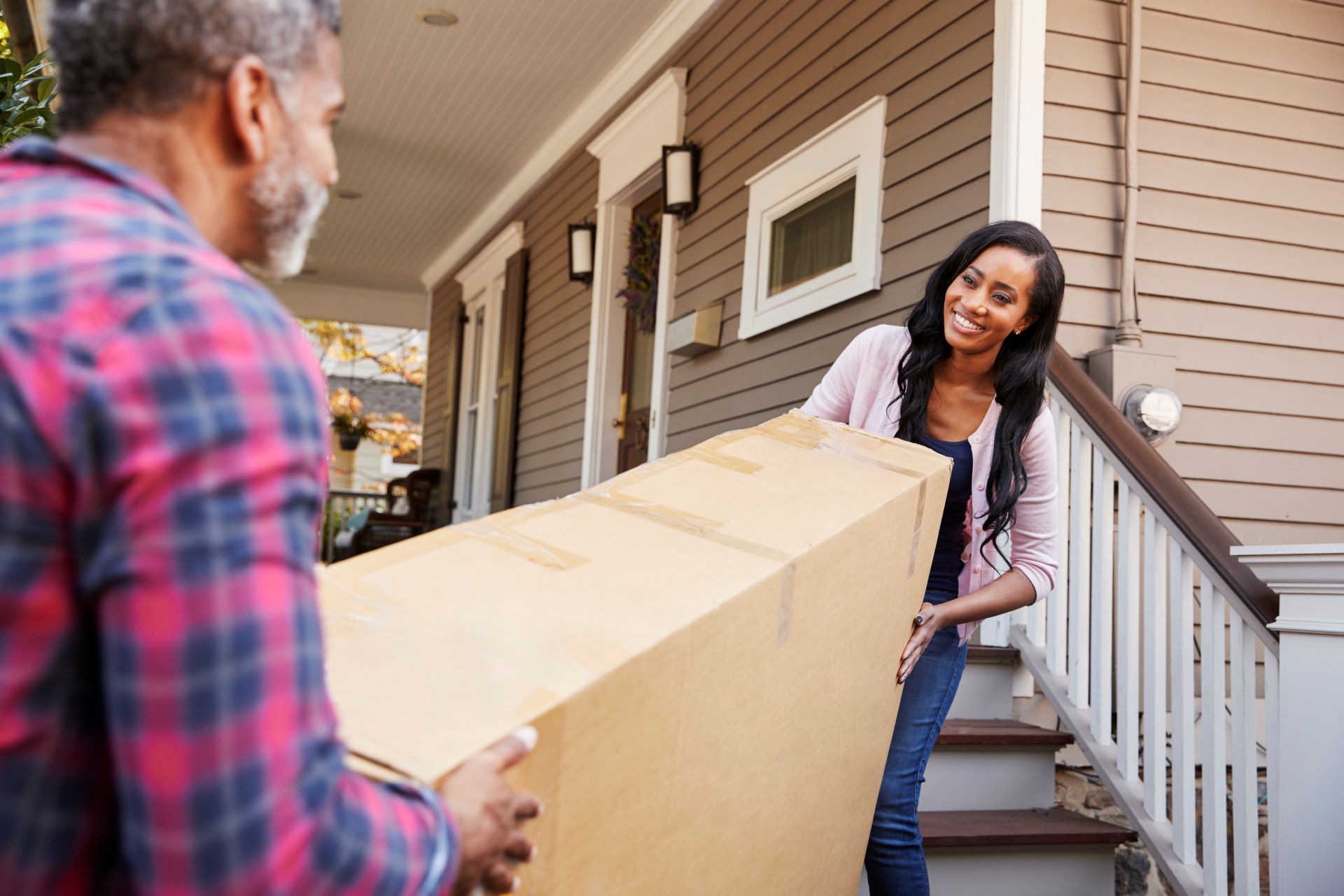 a couple carrying an old tv outside in a box, stepping off porch