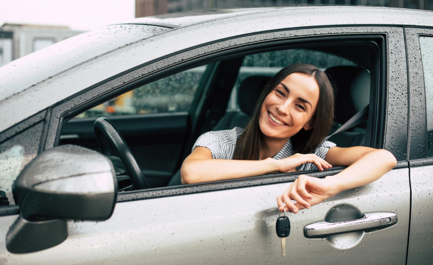 Person smiling and leaning out of a silver car window on a rainy day