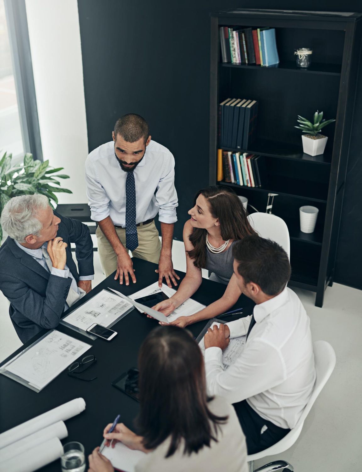 Business team meeting around a table in a modern office, discussing documents with laptops and notes.