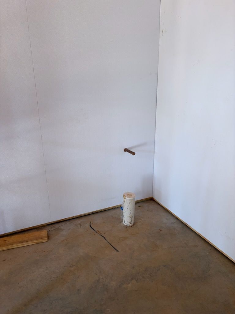 Empty room corner with white walls, concrete floor, a small pipe, and a white canister near the wall.