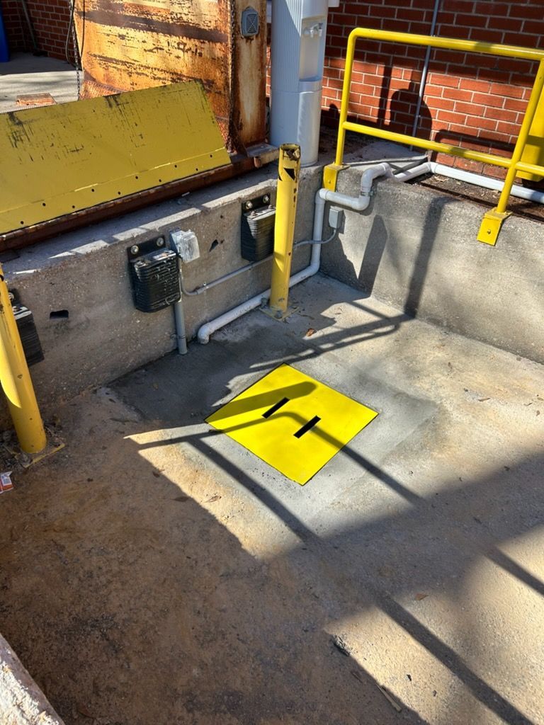 Yellow accessibility platform and railings beside a concrete loading area with a marked floor hatch.