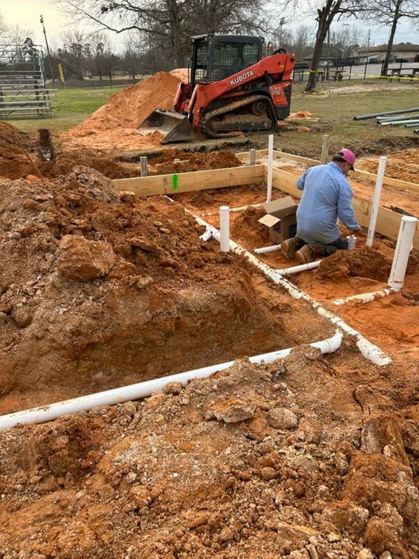 Construction site with excavator and worker installing white PVC pipes in muddy trenches