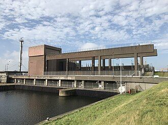 Waterpompstation aan een kanaal met openluchtpaden. Blauwe lucht, groen gras.