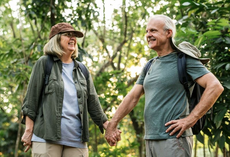 Two hikers smiling and holding hands on a sunlit forest trail