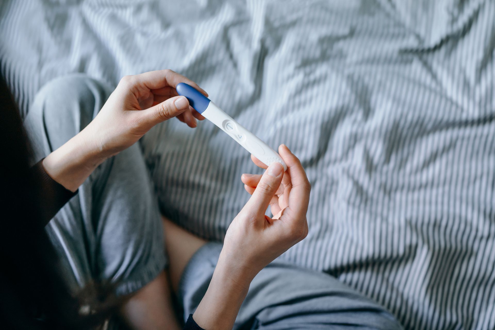 Una donna è seduta su un letto con in mano un test di gravidanza.