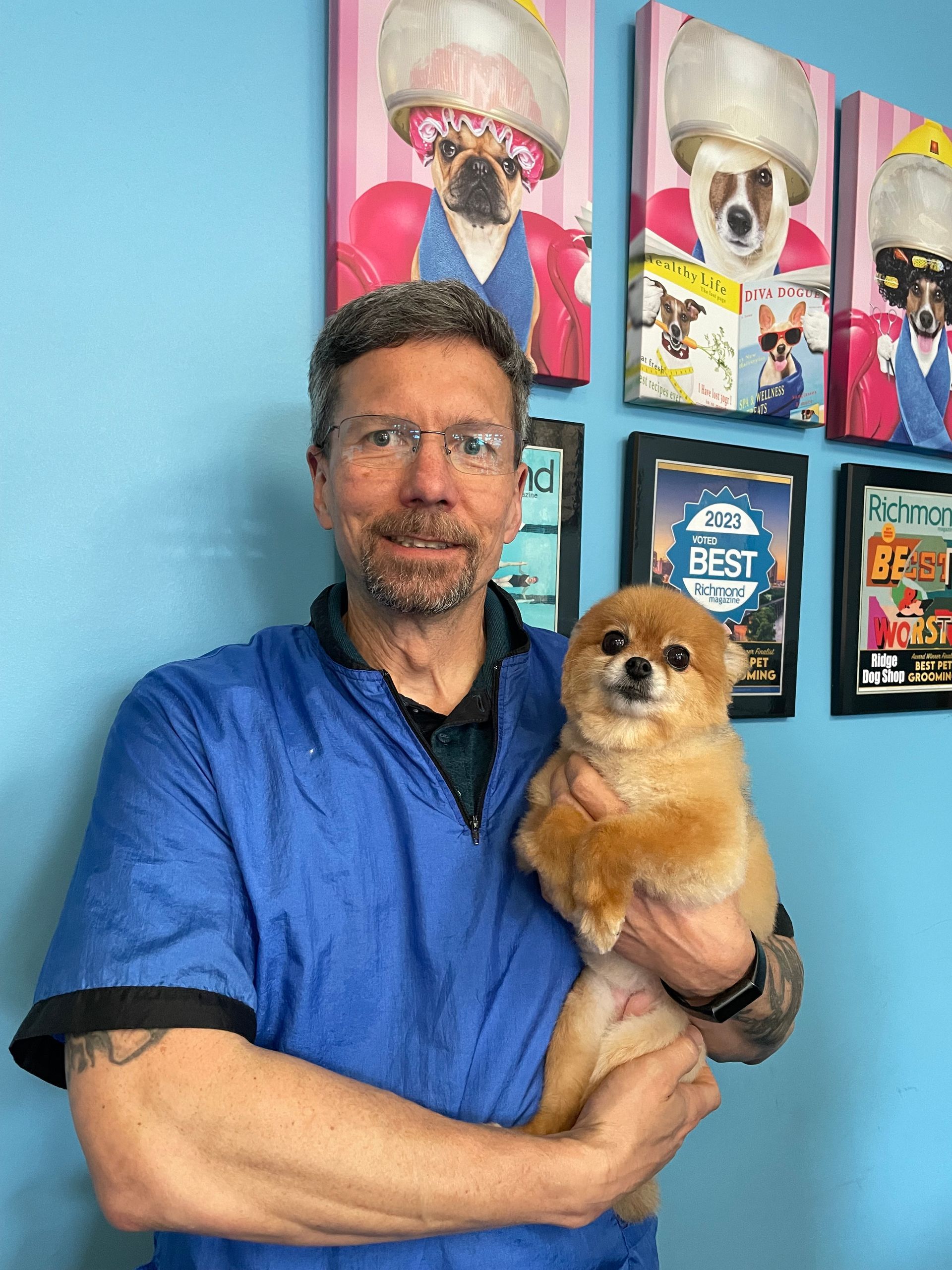 A man is holding a small dog in his arms in front of a wall with pictures of dogs on it.
