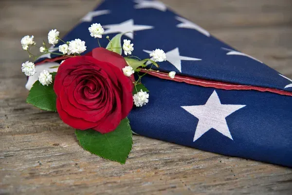 Red rose with baby’s breath on a folded American flag on a wooden surface
