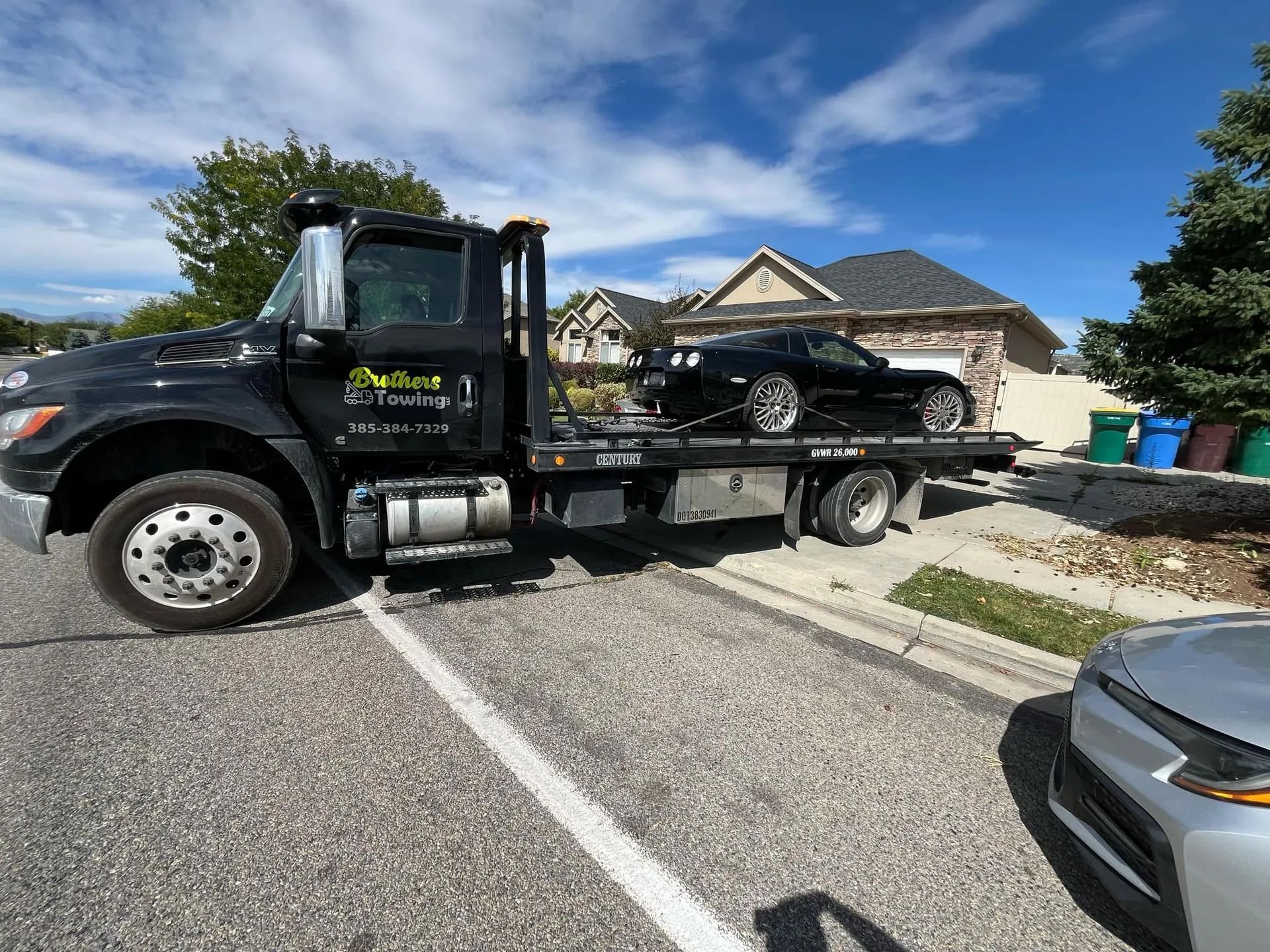 Tow truck hauling a black car on a flatbed in a suburban driveway under a blue sky