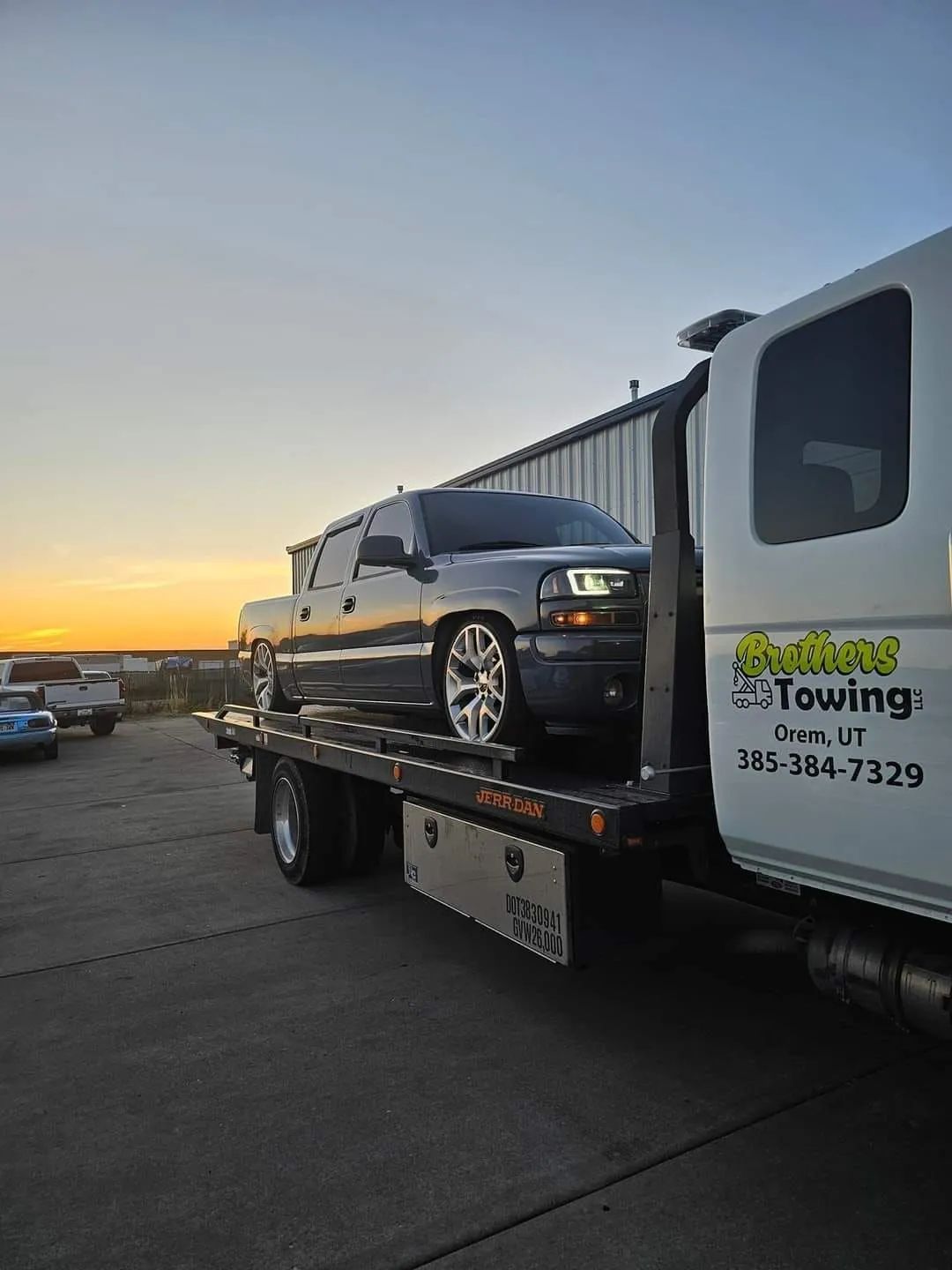 Gray pickup truck on a flatbed tow truck in Oregon, Utah, at sunset.