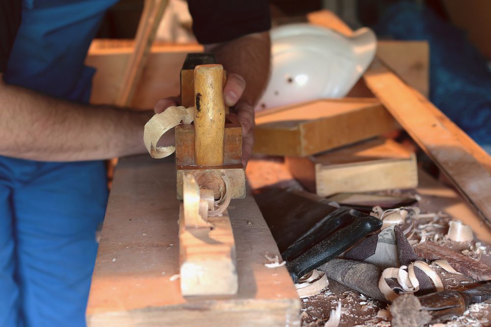 A Man is Using a Plane to Carve a Piece of Wood — Byron Bay Carpentry and Construction In Brunswick Heads, NSW