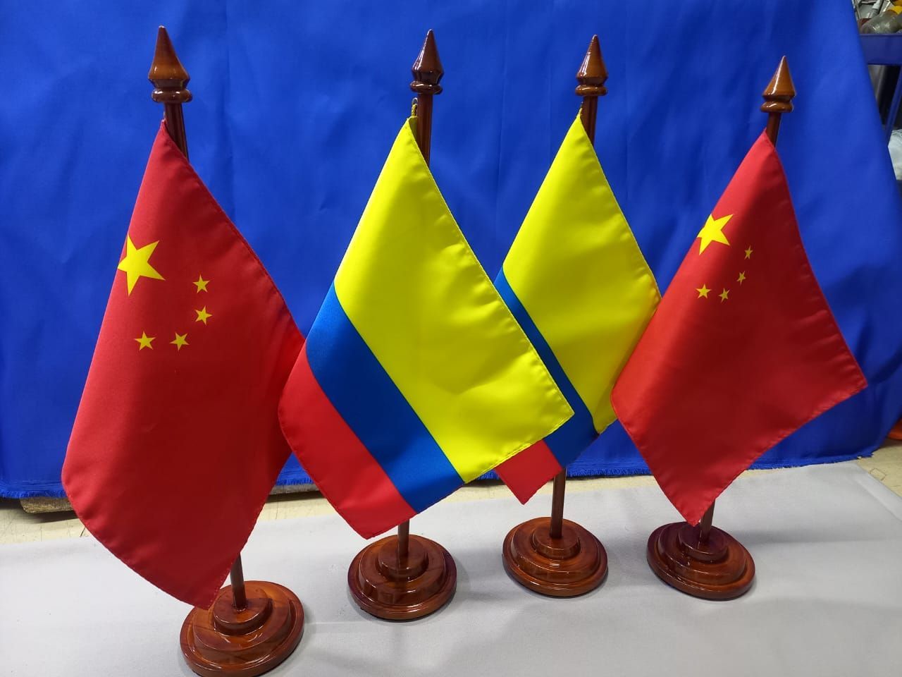 Cuatro banderas de mesa: dos banderas chinas y dos banderas tricolores amarillas, azules y rojas sobre bases de madera.