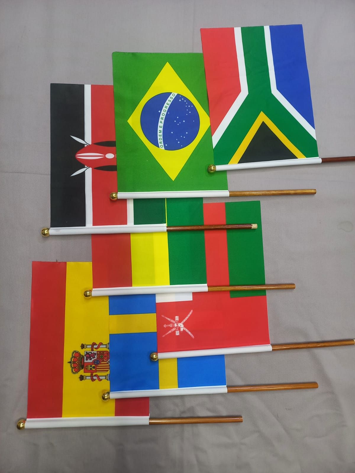 Small arrangement of miniature flags, including Brazil, South Africa, Spain, and Chile, on sticks against a wall.