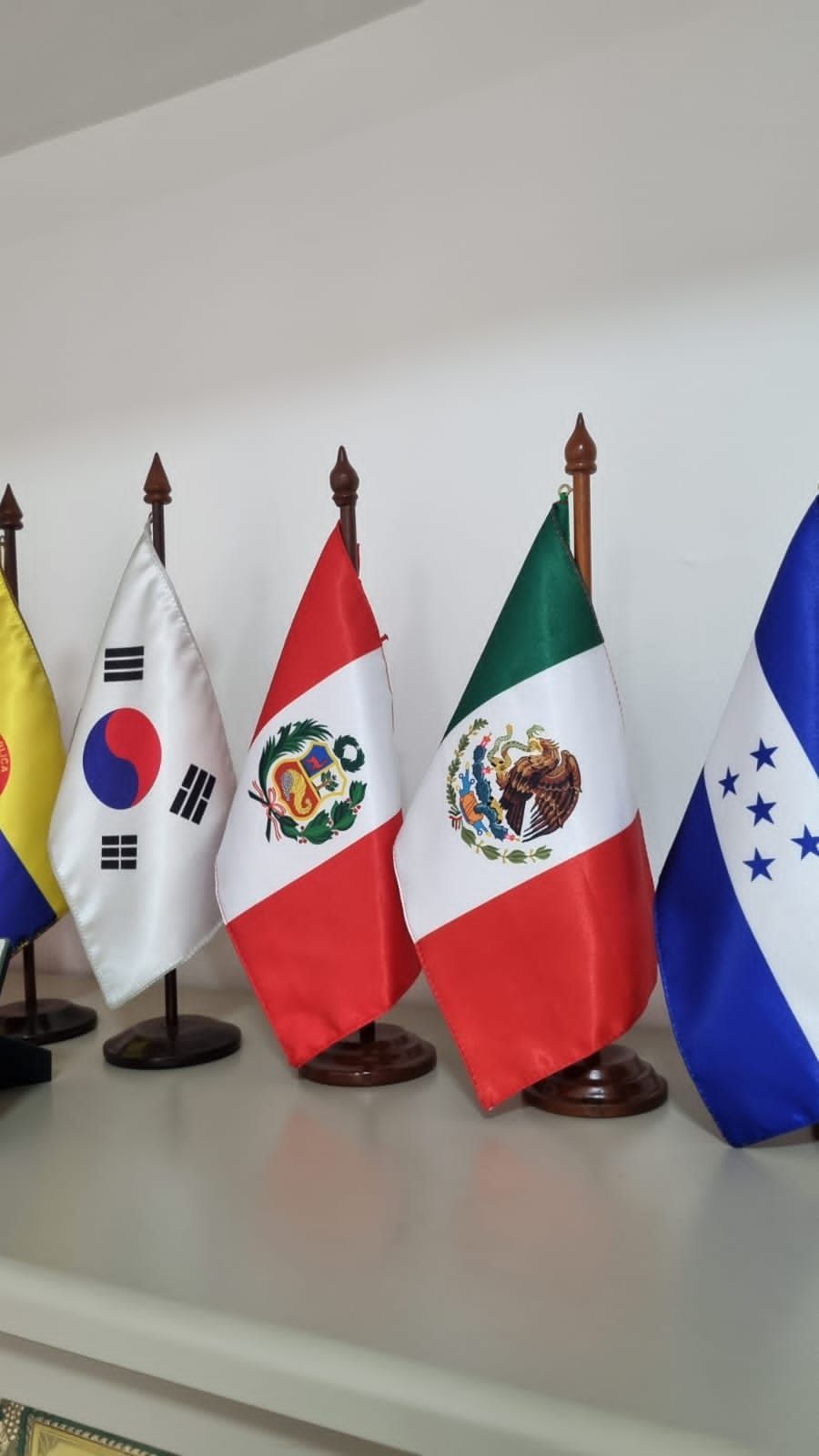 Several small national flags on stands displayed indoors on a shelf, including South Korea, Peru, Mexico, and Honduras.