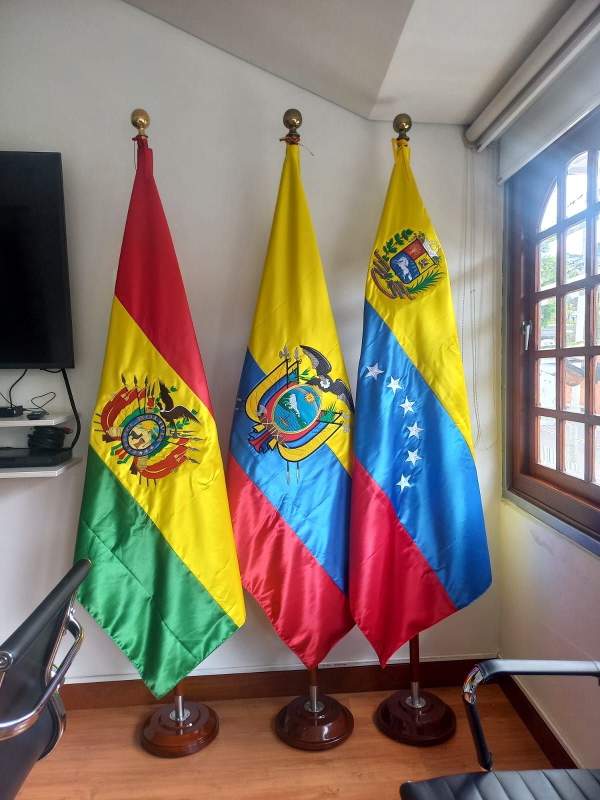 Three Bolivian flags on stands displayed indoors near a window