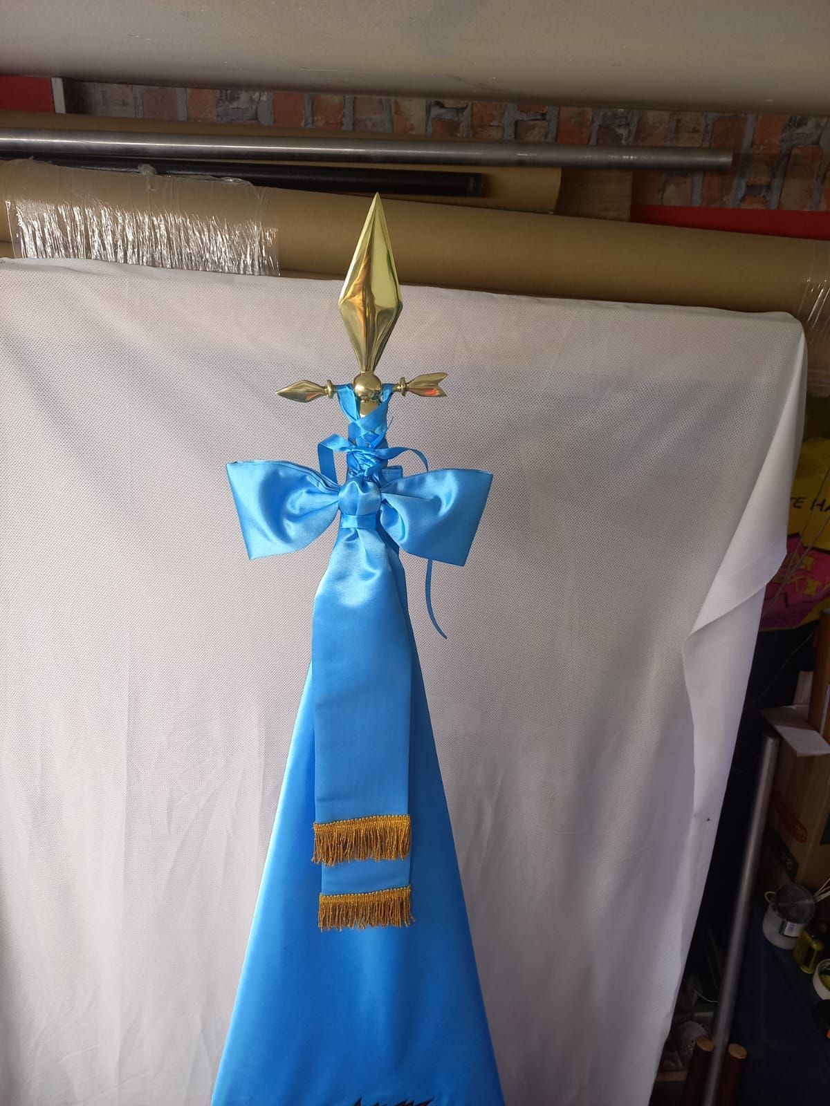 Blue ceremonial staff with a gold spear tip and ribbon accents, standing against a white backdrop