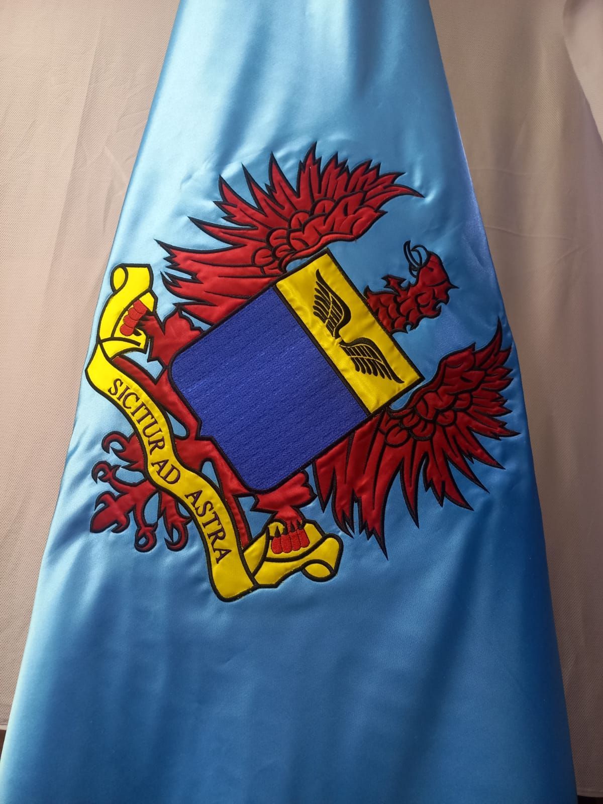 Blue fabric with a red-and-yellow heraldic crest embroidered on it