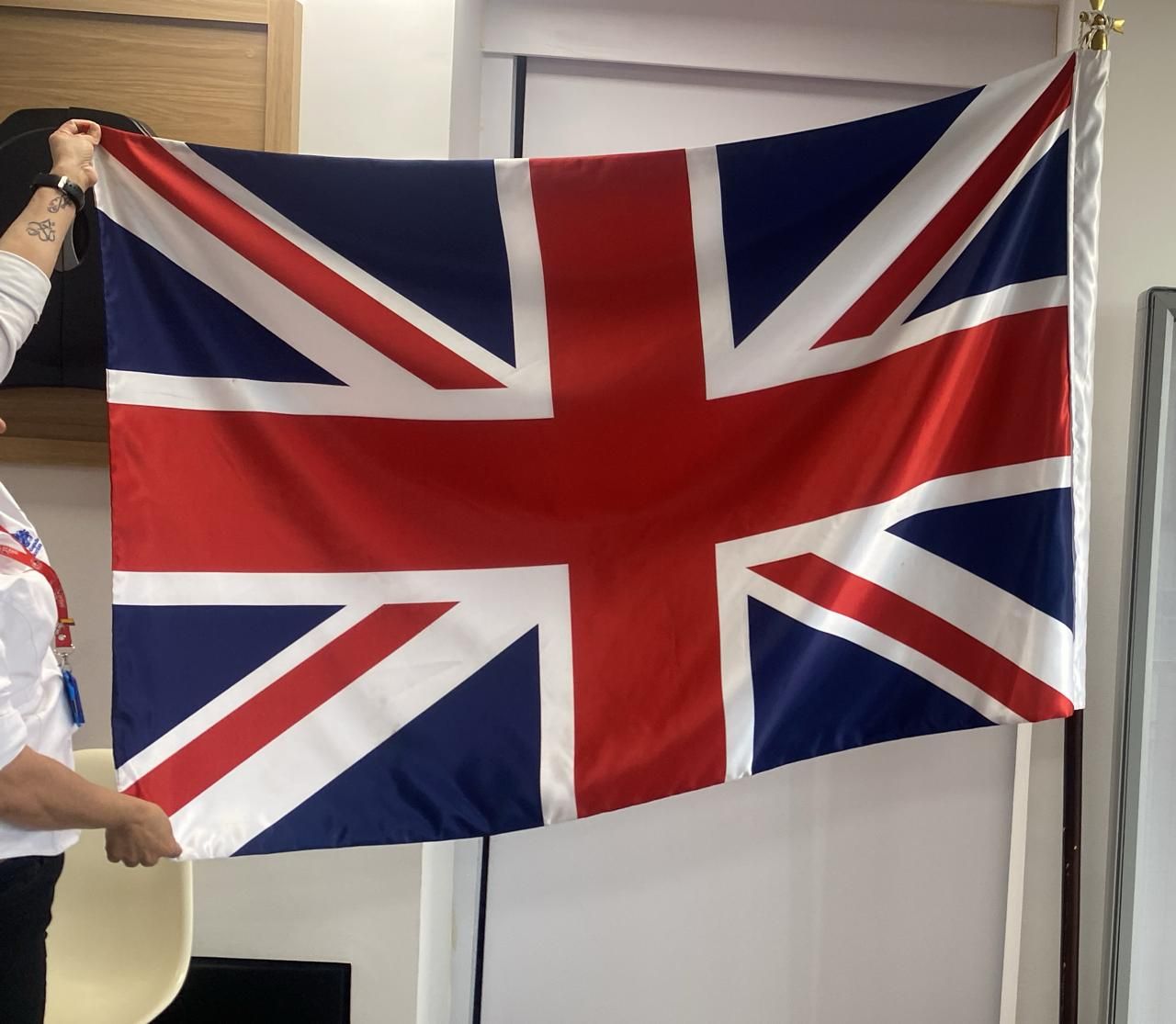 Union Jack flag hanging indoors, held up by a person at the left edge.