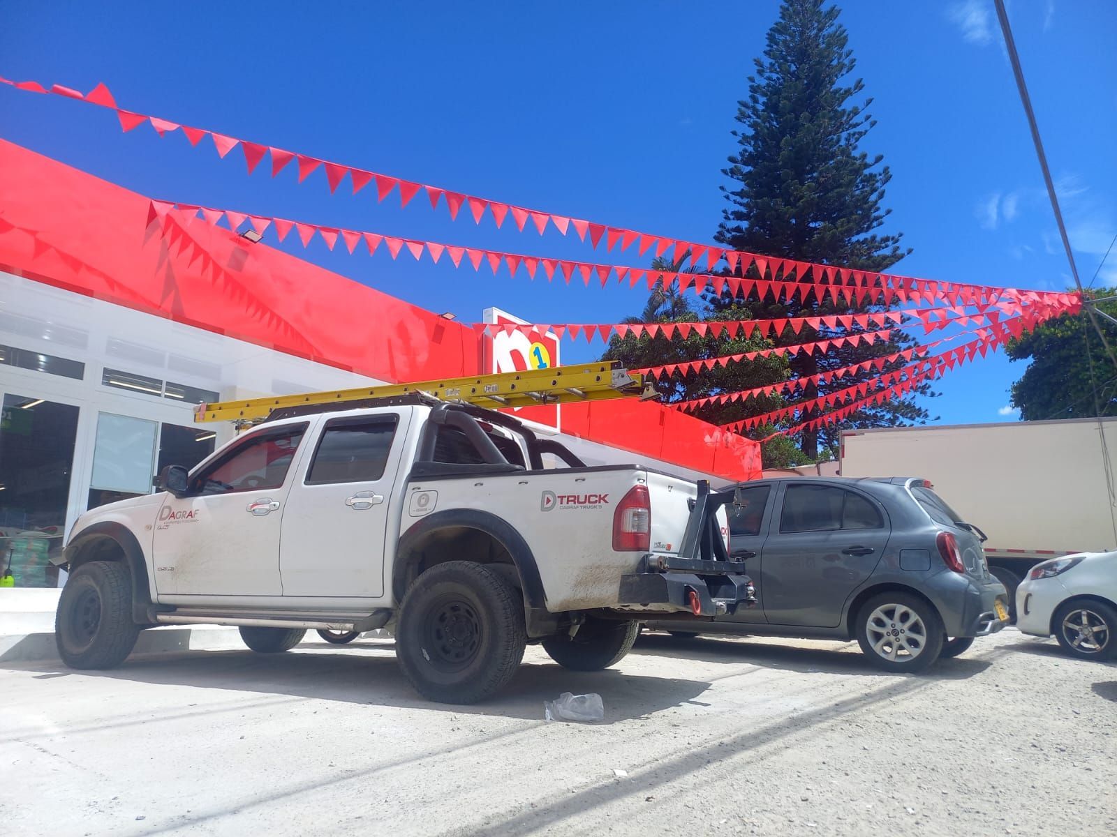 Parked white pickup and gray SUV under red pennant flags in a sunny lot