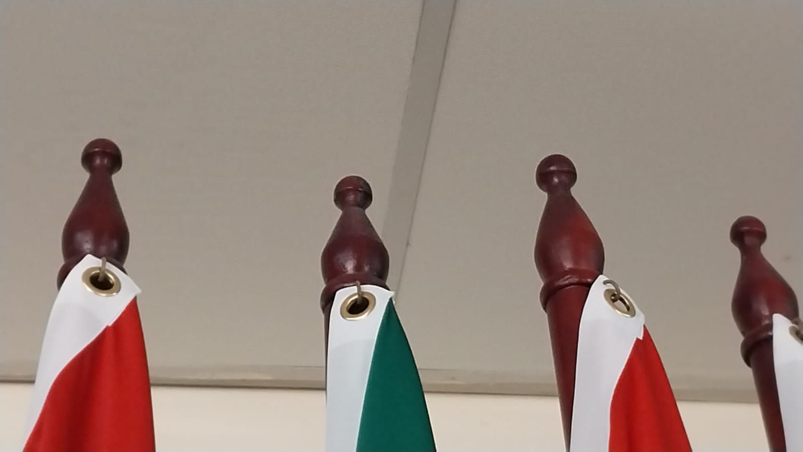 Three red-topped flagpoles with hanging red, white, and green flags against a ceiling.