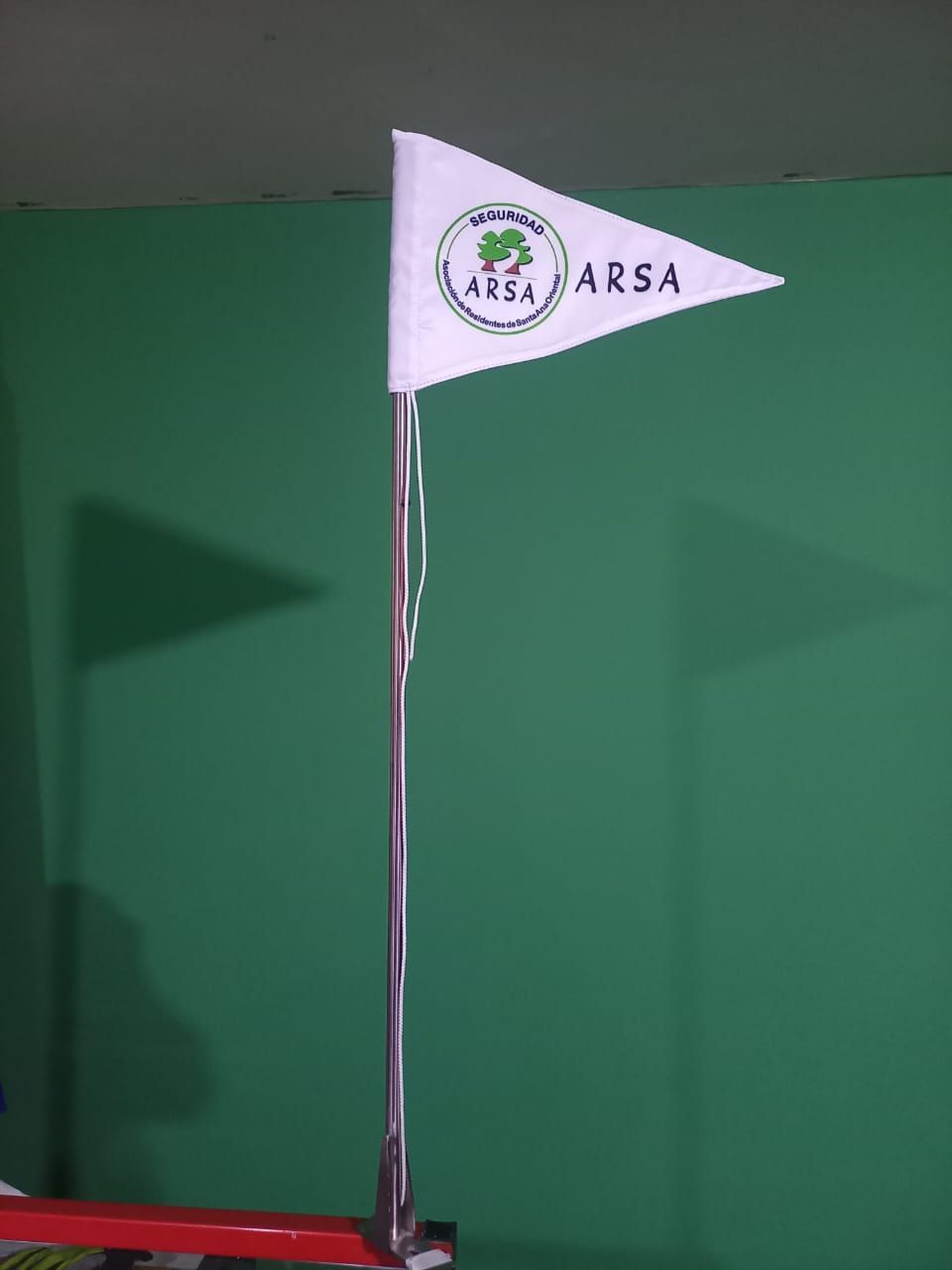 White ARSA flag on a metal pole against a green wall.