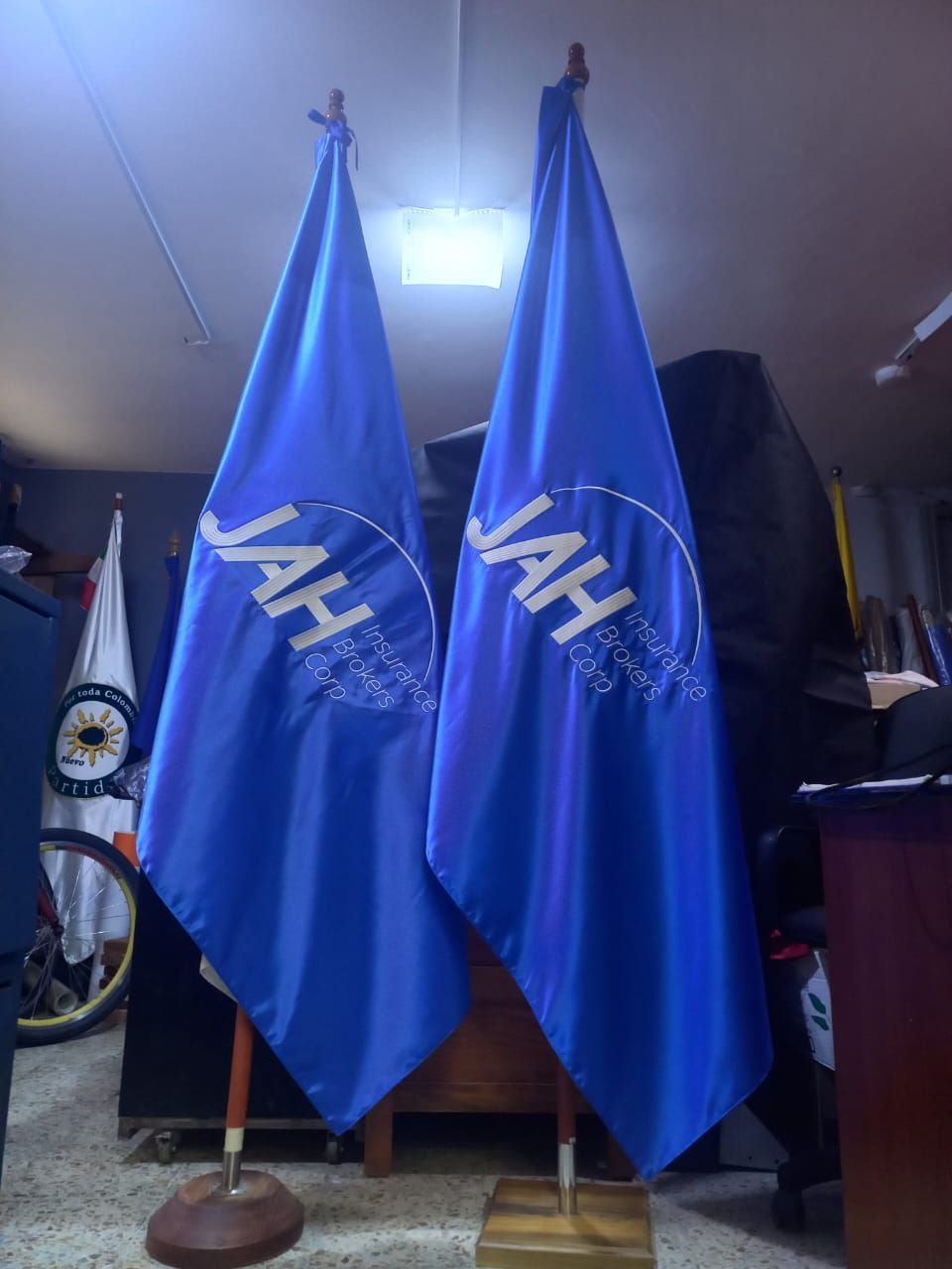 Two blue JAH flags on poles indoors, with a bright ceiling light overhead.