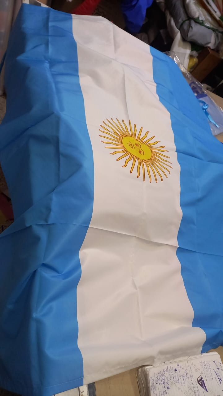 Argentine flag draped over a surface, showing light blue, white, and a yellow sun emblem.
