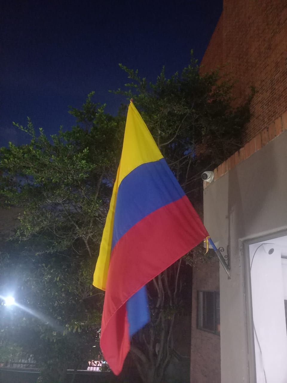 Colombian flag hanging outdoors at night beside a building and tree