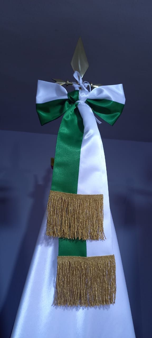Green, white, and blue ribbon decoration with two gold tassels hanging on a wall.
