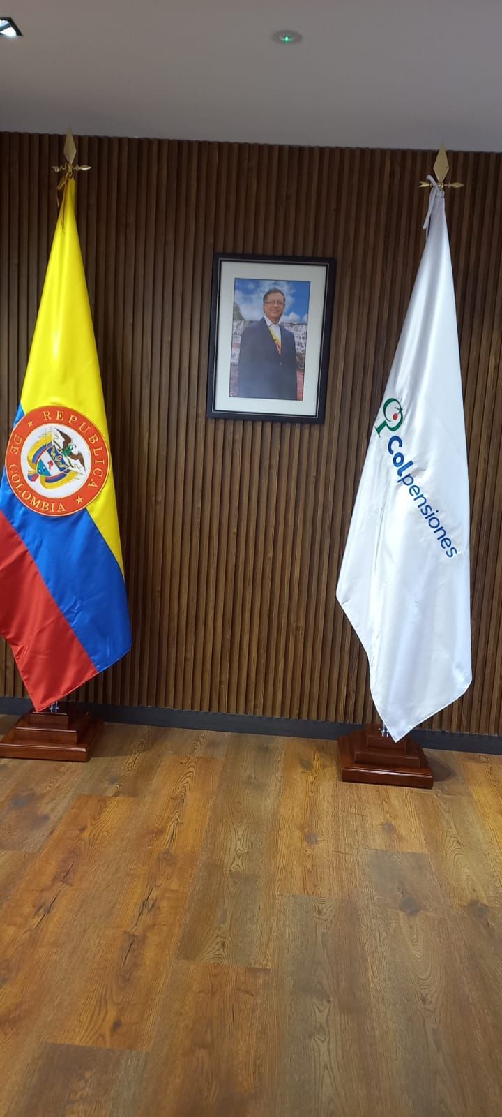 Colombian and white flags beside a framed portrait in a wood-paneled room