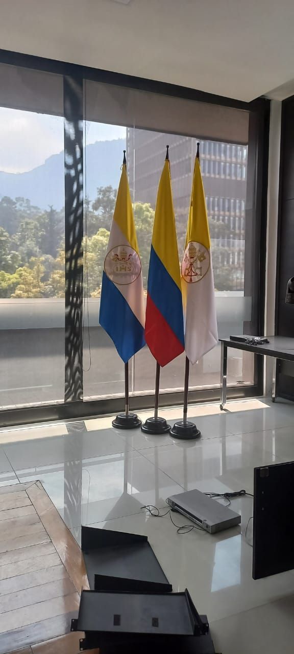 Three flags on stands in a bright room with large windows and a city view.