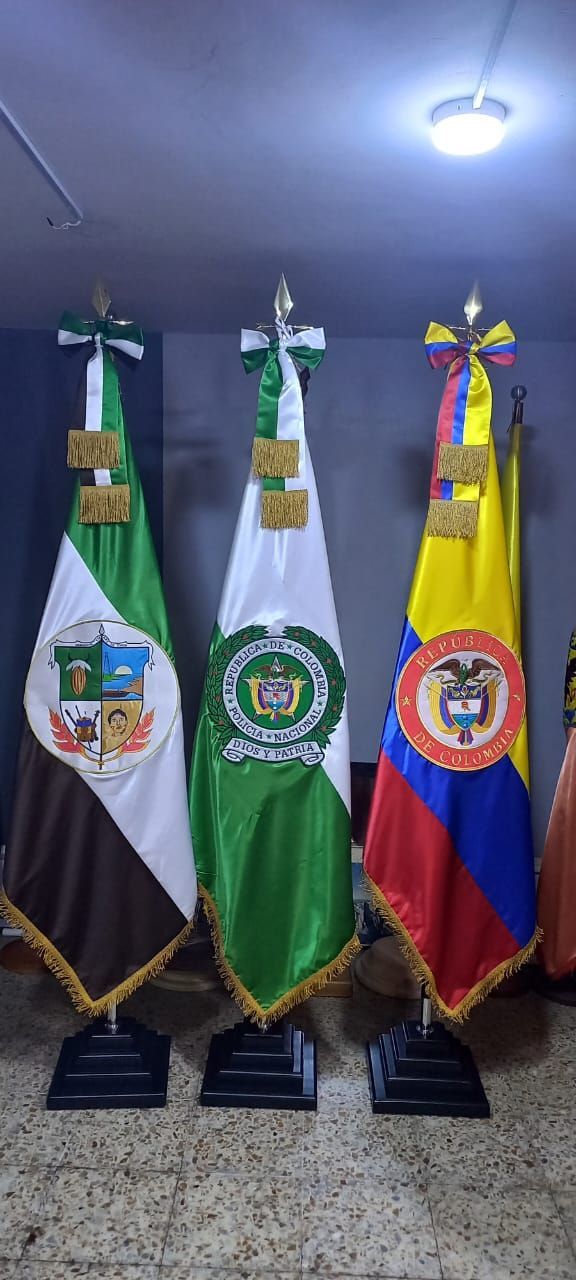 Three standing flags: white, green, and yellow-red-blue, displayed indoors on bases.