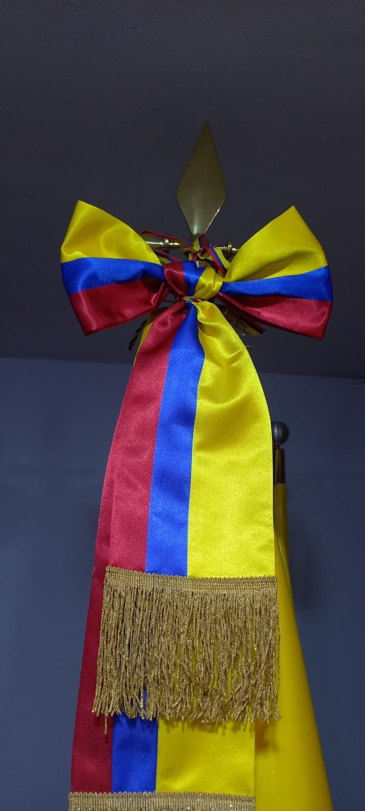 Blue, yellow, and red ribbon bow with long streamers and a gold fringe hanging indoors